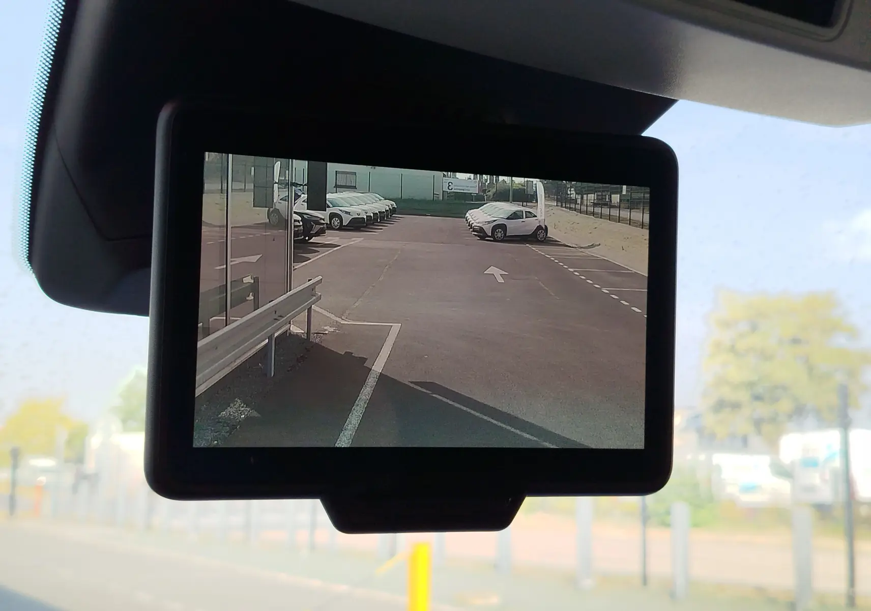 Vue de l'écran de caméra de recul du Renault Kangoo 2023 montrant un parking avec plusieurs véhicules blancs.