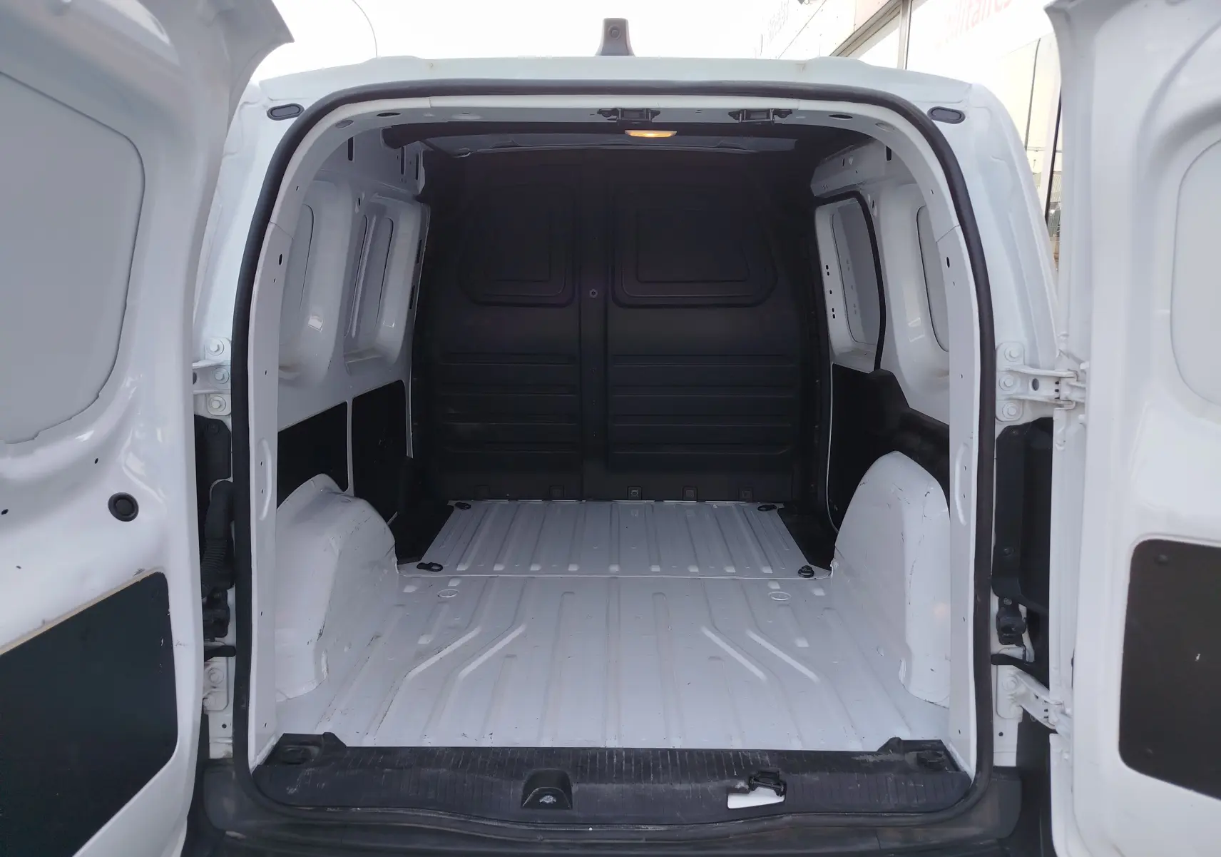 Vue arrière ouverte du Renault Kangoo blanc minéral 2023, montrant l'espace de chargement vide et les portes battantes.