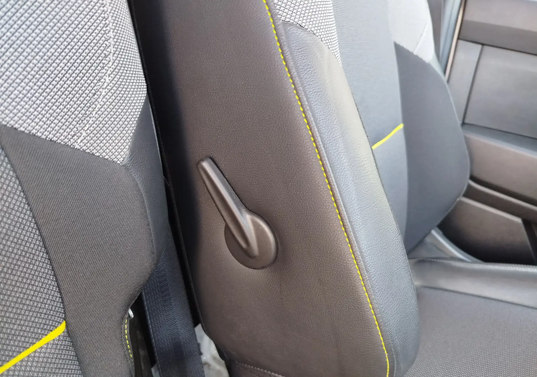 Détail de la manette de réglage latérale sur le siège avant gris foncé avec surpiqûres jaunes du Renault Kangoo blanc.