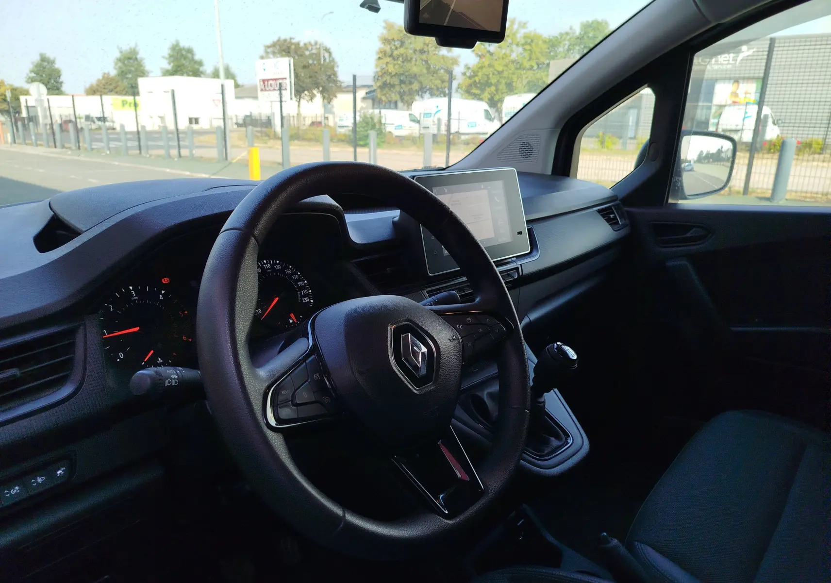 Vue intérieure côté conducteur du Renault Kangoo 2023, volant multifonction et écran tactile central visibles.