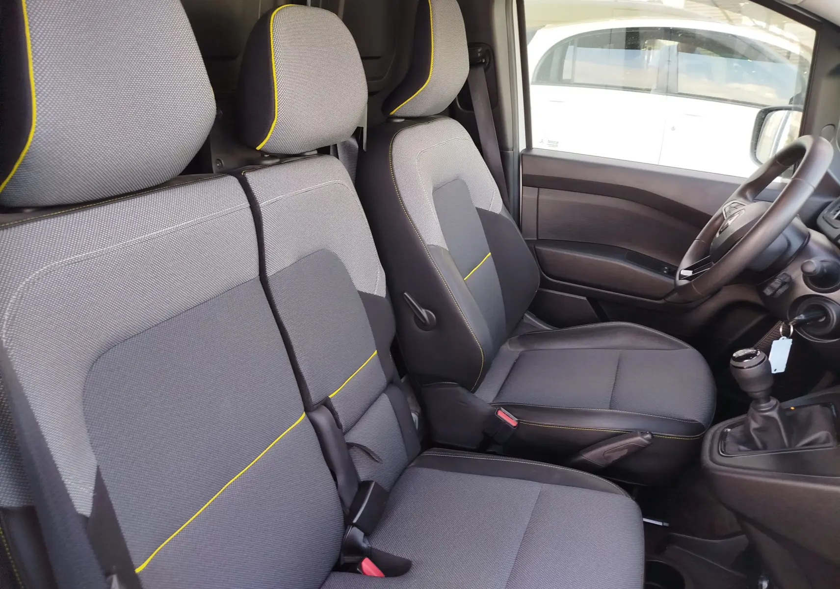 Vue intérieure côté conducteur du Renault Kangoo 2023, sièges gris avec surpiqûres jaunes et volant multifonction.