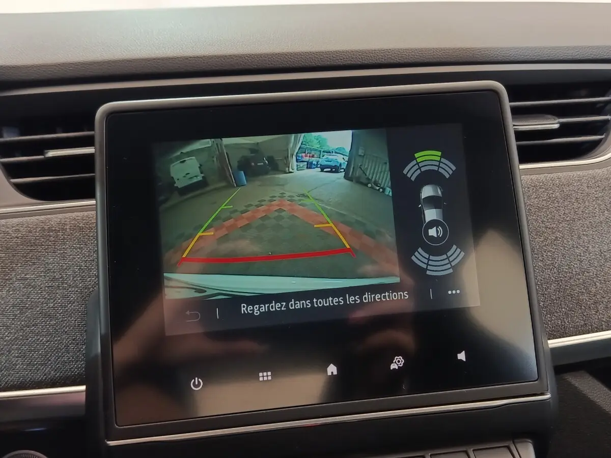 Écran tactile central montrant la caméra de recul et l’aide au stationnement arrière d’une Renault ZOE blanche.