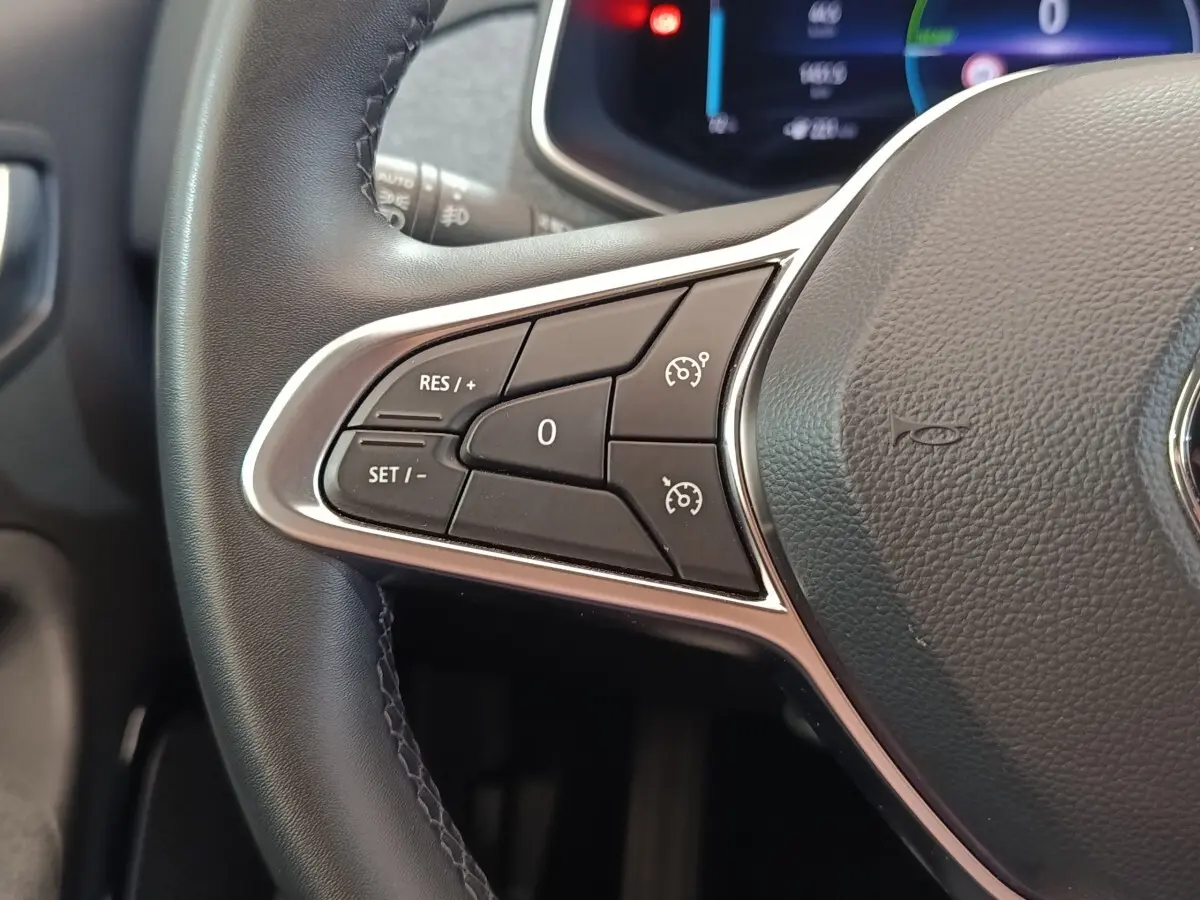 Gros plan sur les commandes de régulateur de vitesse au volant cuir noir d’une Renault ZOE Intens blanc.
