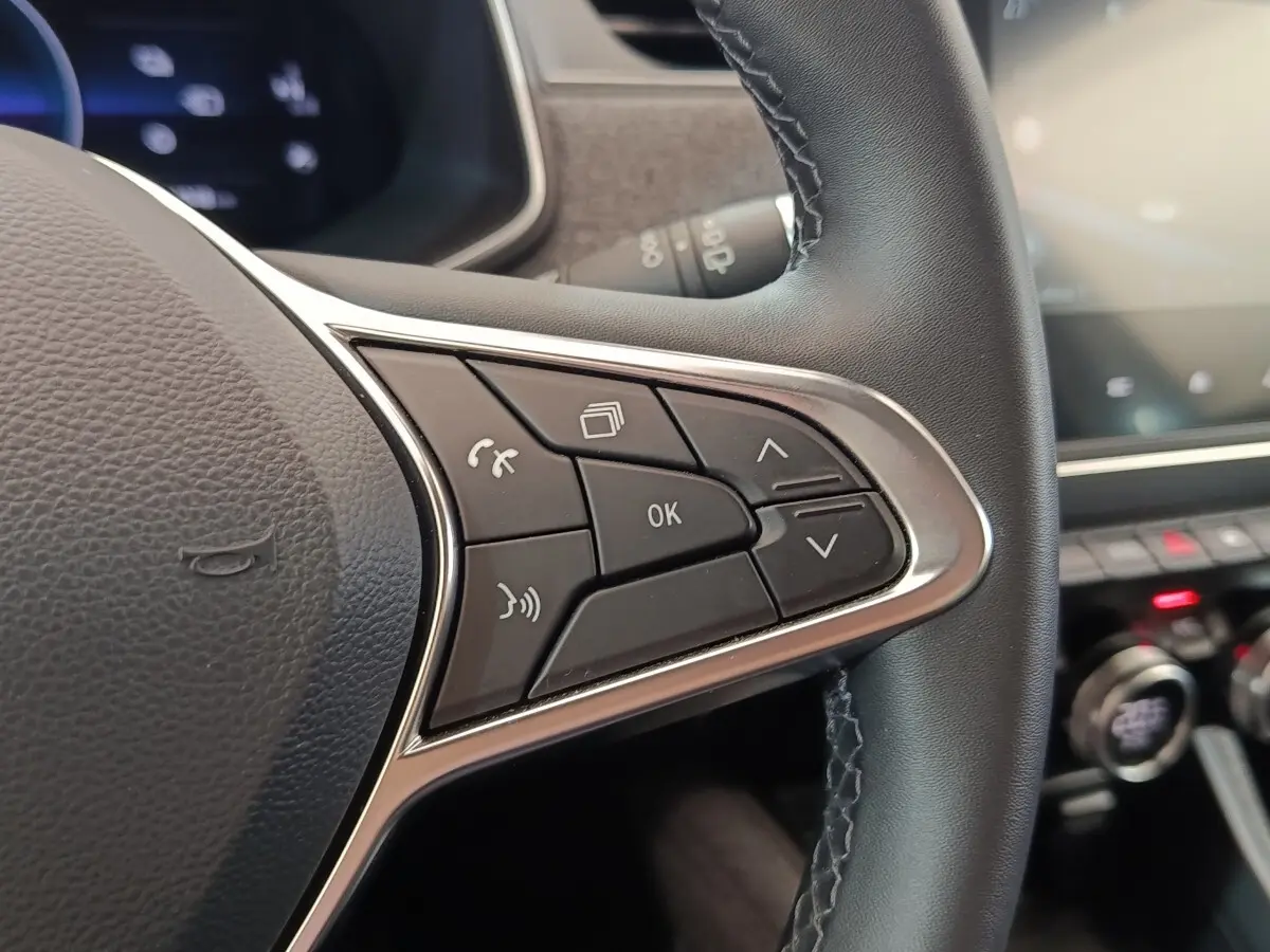 Gros plan sur les commandes multifonctions à droite du volant cuir noir de la Renault ZOE Intens blanc, tableau de bord en arrière-plan flou.