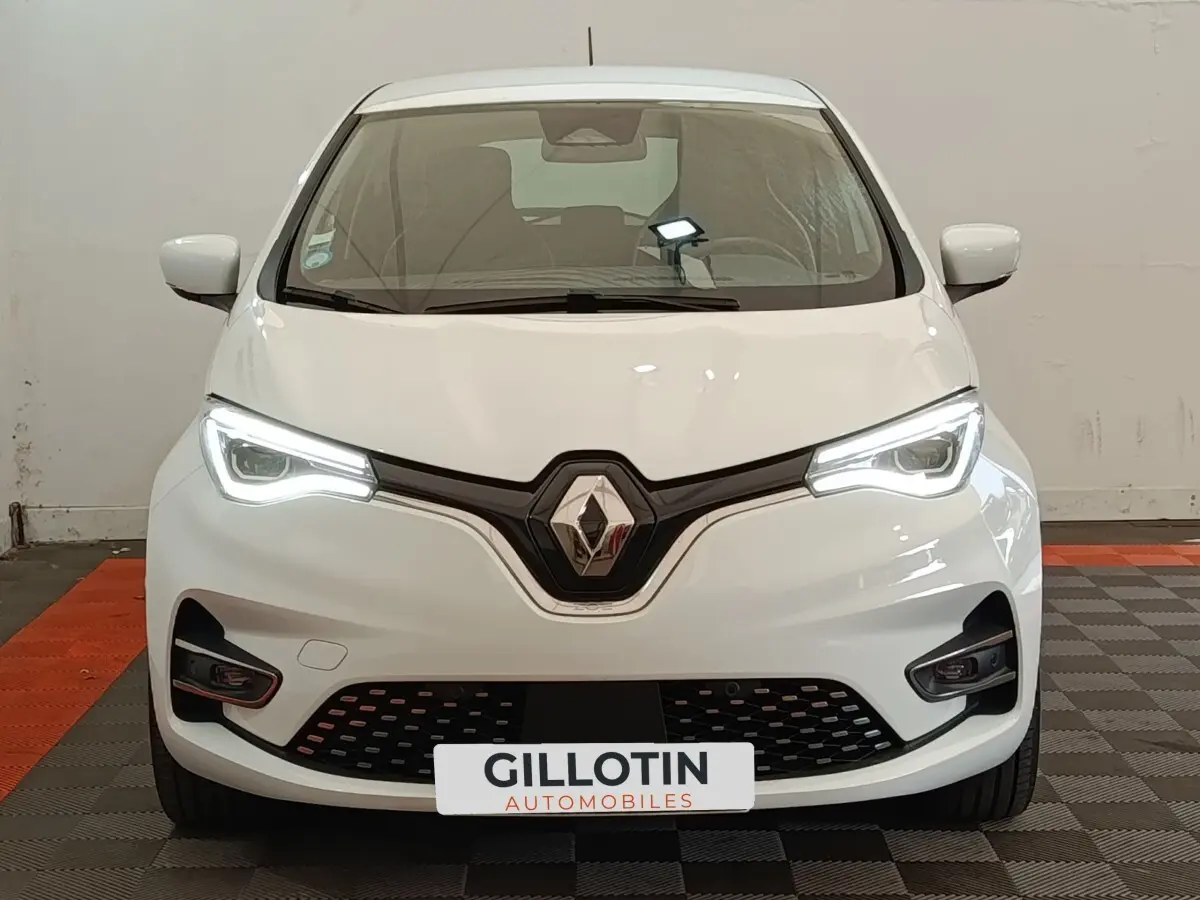 Vue frontale d'une Renault ZOE Intens R110 blanche avec phares LED allumés et calandre noire distinctive.