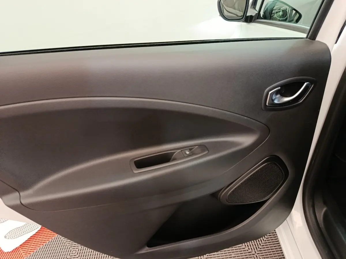 Vue intérieure de la porte avant droite noire de la Renault ZOE Intens R110 blanche, avec poignée et haut-parleur intégré.
