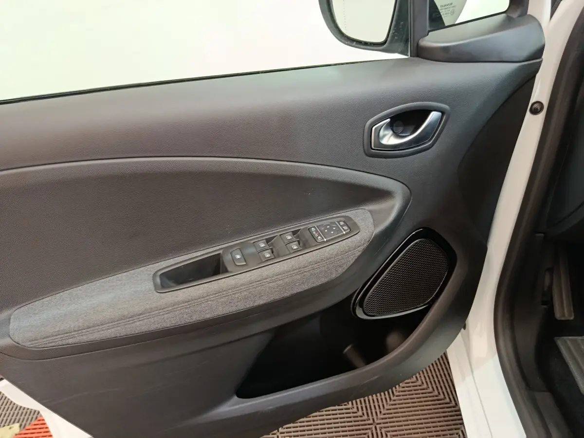 Vue intérieure côté gauche de la porte avant blanche de la Renault ZOE Intens avec commandes électriques et haut-parleur intégré.