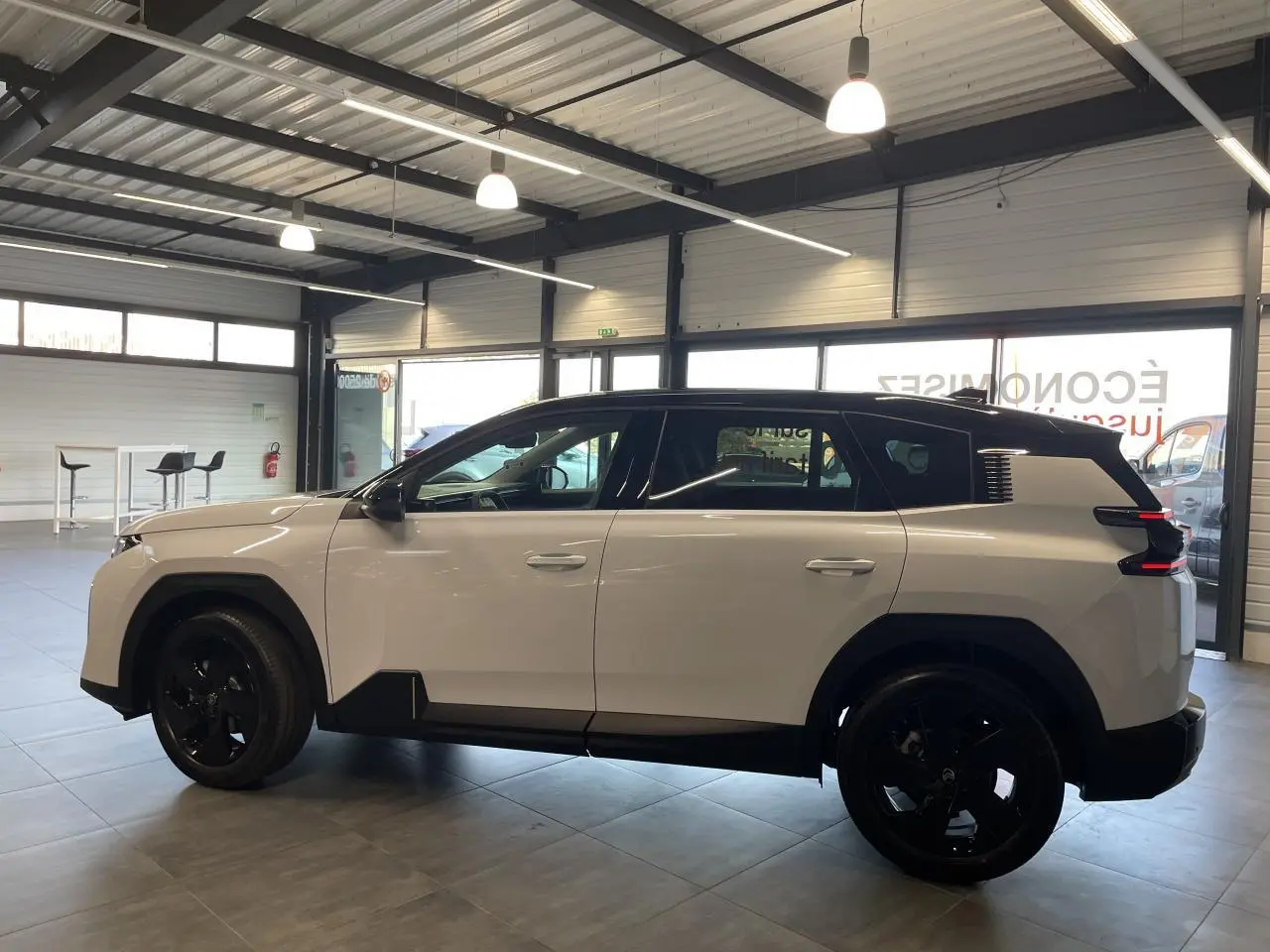 Vue de profil côté gauche d'un Citroën C5 Aircross blanc Okenite avec toit noir et jantes noires en intérieur showroom.