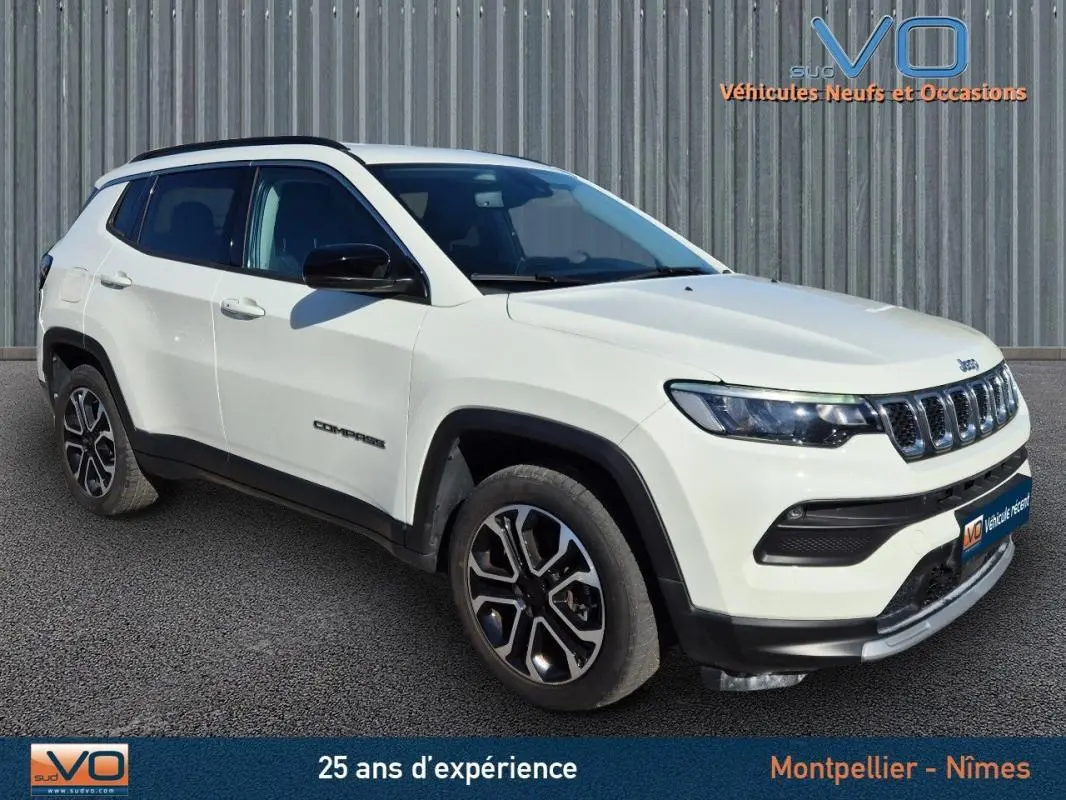 Vue 3/4 avant droit d'un Jeep Compass blanc avec barres de toit et jantes 18 pouces, sur fond industriel.