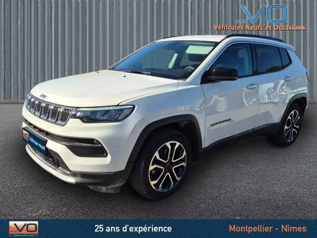 Jeep Compass blanc vu en 3/4 avant droit, avec jantes 18 pouces et barres de toit visibles.