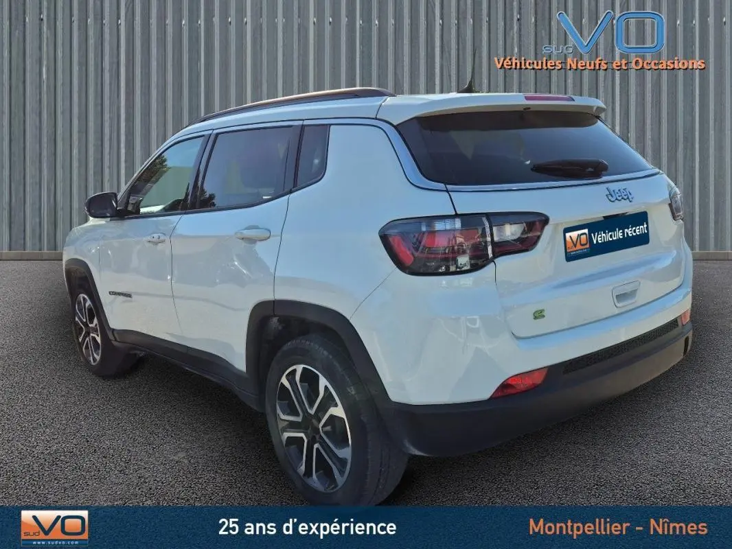Vue 3/4 arrière gauche d'un Jeep Compass blanc 2023 avec barres de toit et jantes 18 pouces.