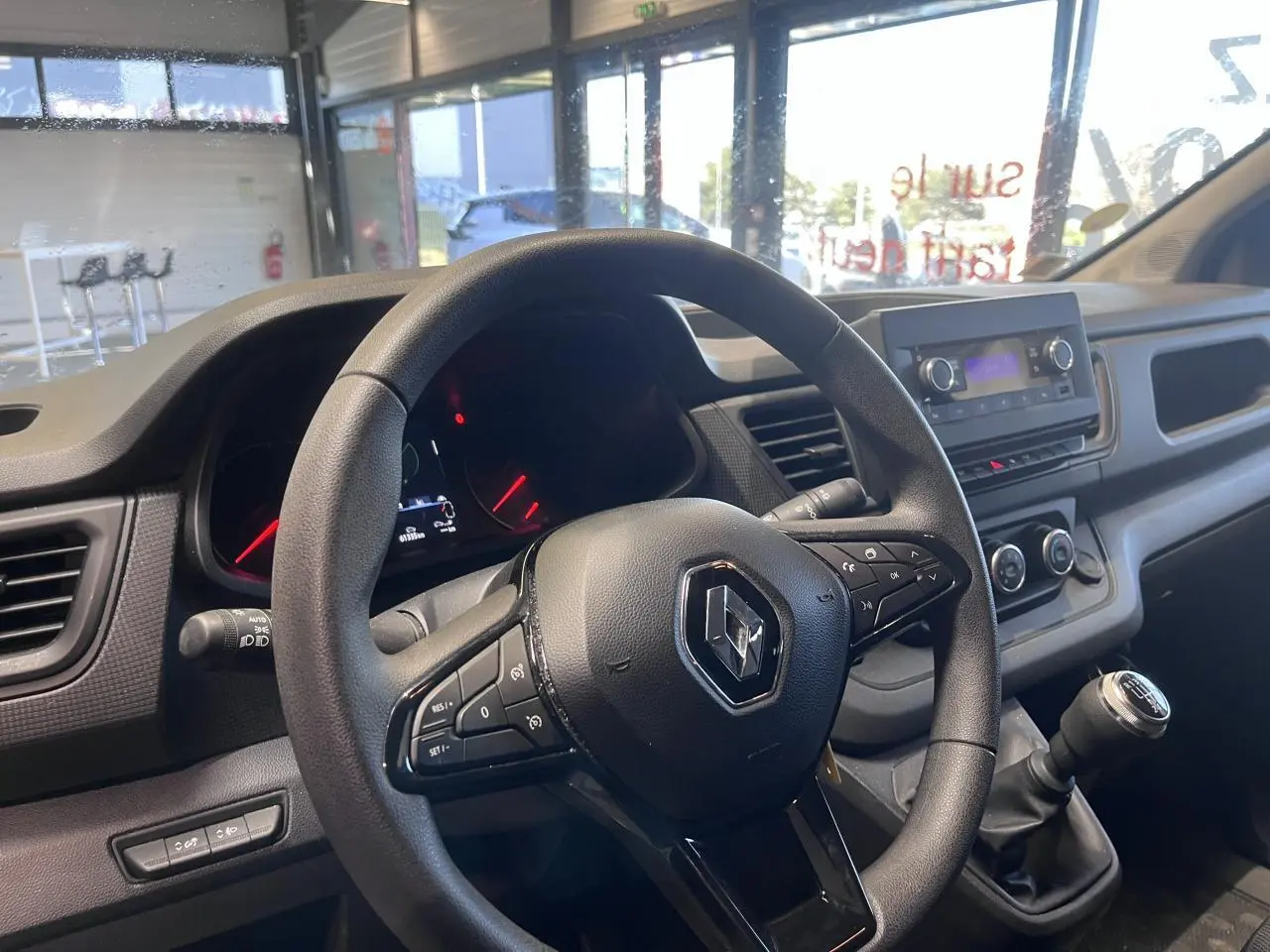 Vue intérieure centrée sur le volant et tableau de bord du Renault Trafic Fourgon gris foncé, avec levier de vitesse manuel.