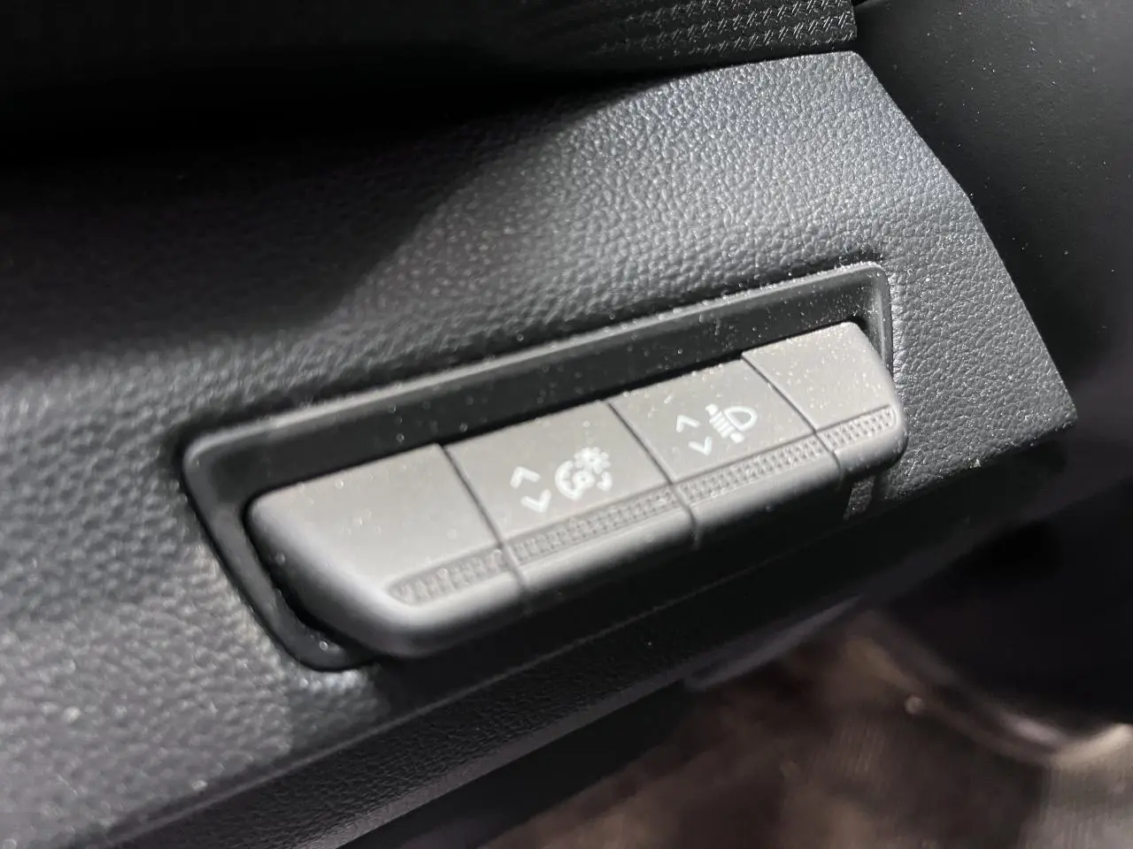 Gros plan sur les commandes de réglage des phares et du tableau de bord du Renault Trafic Fourgon gris foncé.