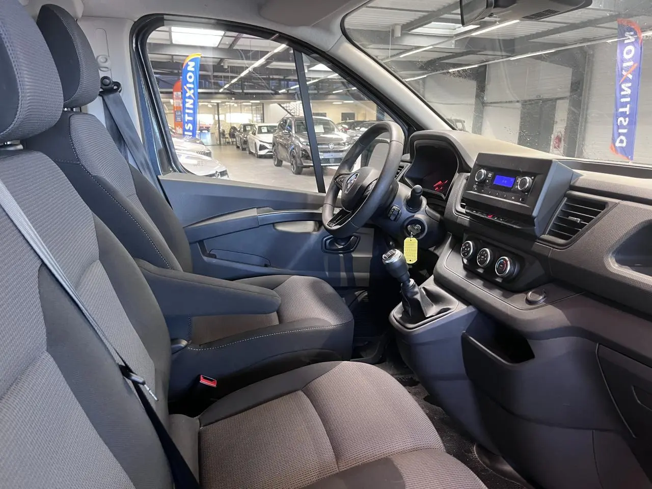 Vue intérieure côté conducteur du Renault Trafic Fourgon 2023, montrant sièges tissu gris et tableau de bord fonctionnel.