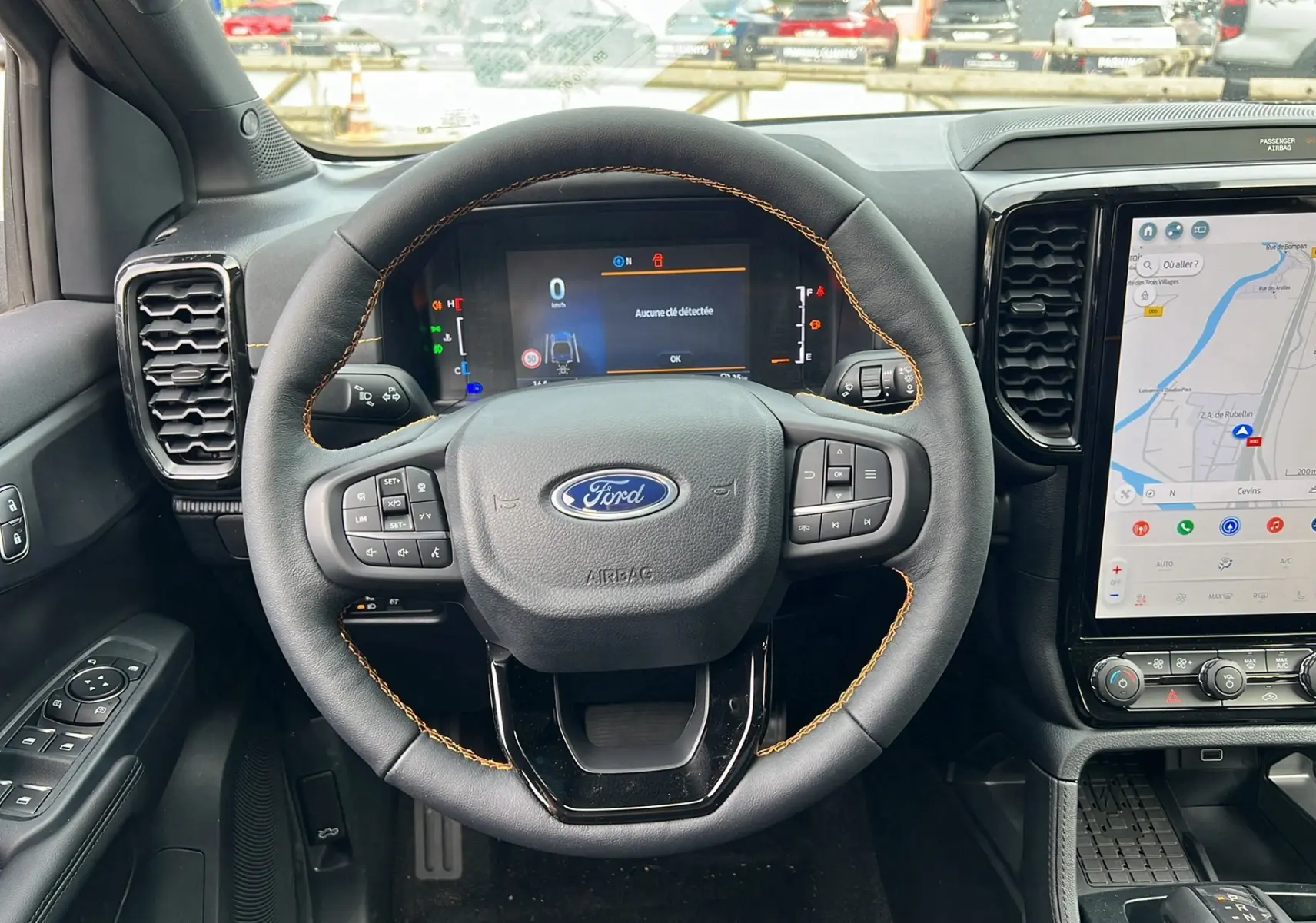 Vue intérieure centrée sur le volant cuir noir avec surpiqûres orange et tableau de bord digital du Ford Ranger Wildtrak 2026.