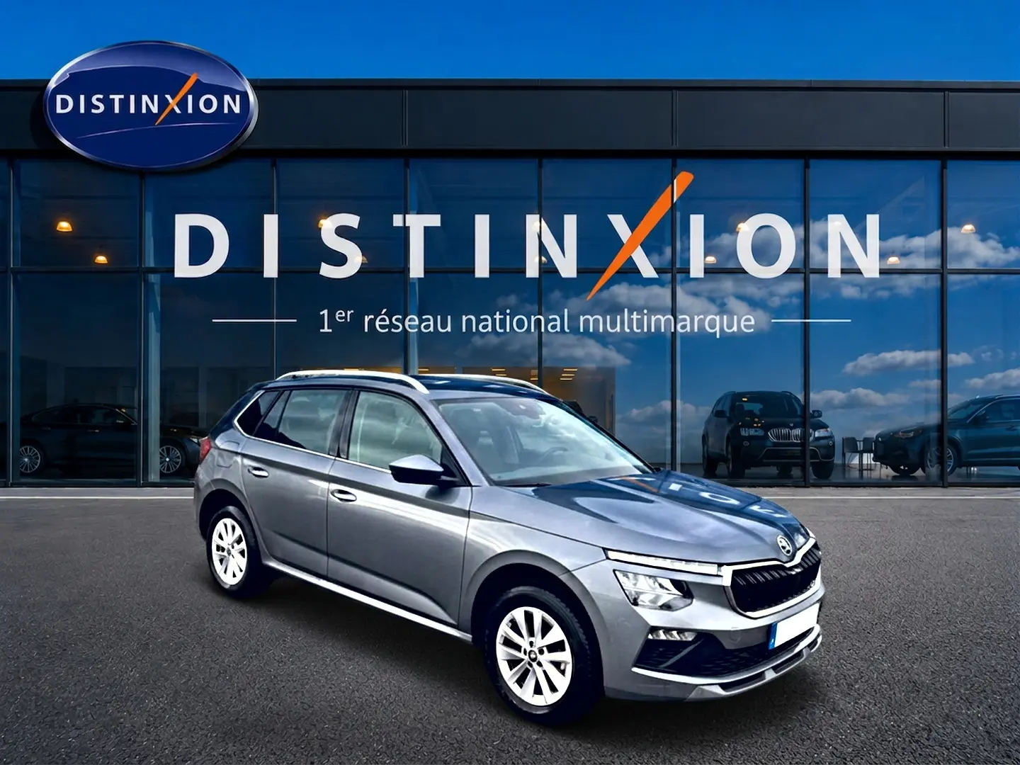 Vue 3/4 avant droit d'un Skoda Kamiq gris métallisé devant une vitrine avec logo Distinxion.