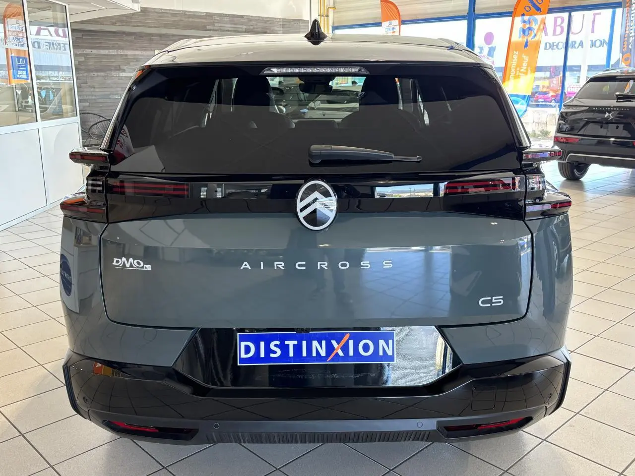 Vue arrière d'un Citroën C5 Aircross vert métallisé avec bandeau noir brillant et feux arrière LED 3D en intérieur showroom.