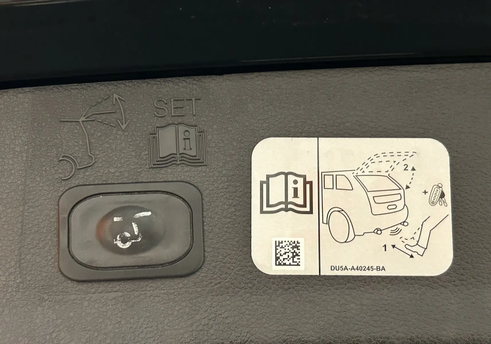Gros plan sur le bouton de réglage du hayon électrique et l'autocollant explicatif à l'intérieur du coffre noir du Ford Kuga.