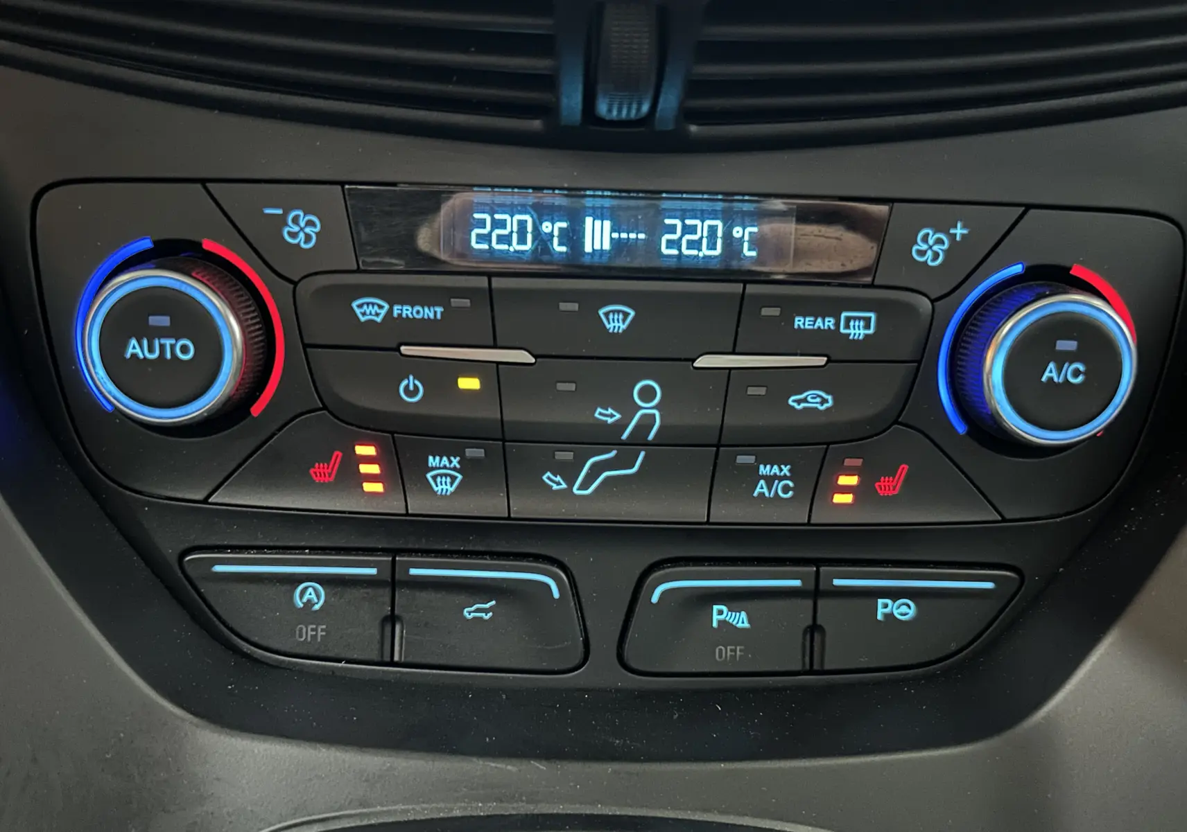Gros plan sur la console de climatisation digitale du Ford Kuga noir, avec réglages chauffants et affichage à 22°C.
