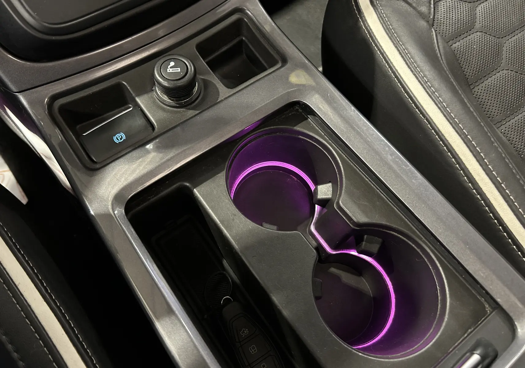 Gros plan intérieur sur la console centrale noire du Ford Kuga 2017, avec porte-gobelets éclairés en violet et sellerie cuir noire.