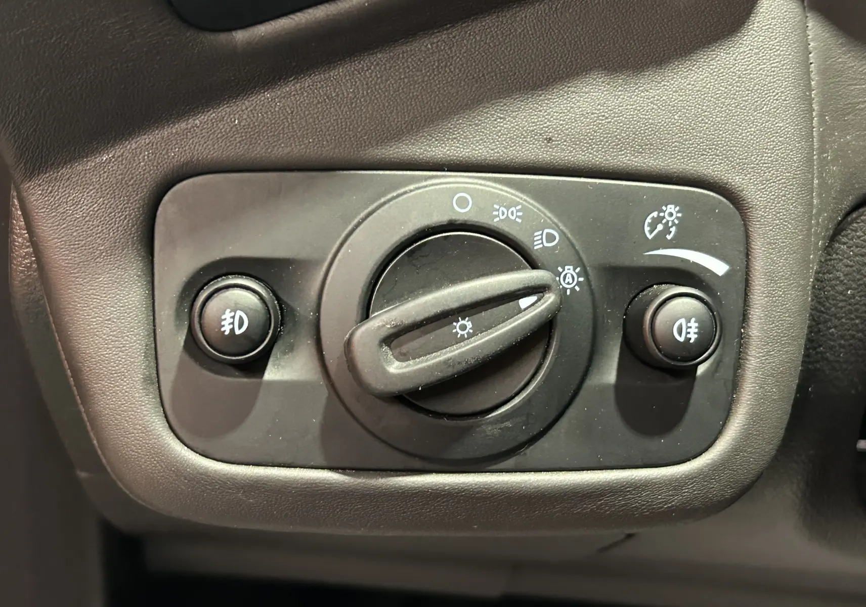 Gros plan sur la commande d’éclairage noire du tableau de bord d’un Ford Kuga noir, avec boutons et molette.