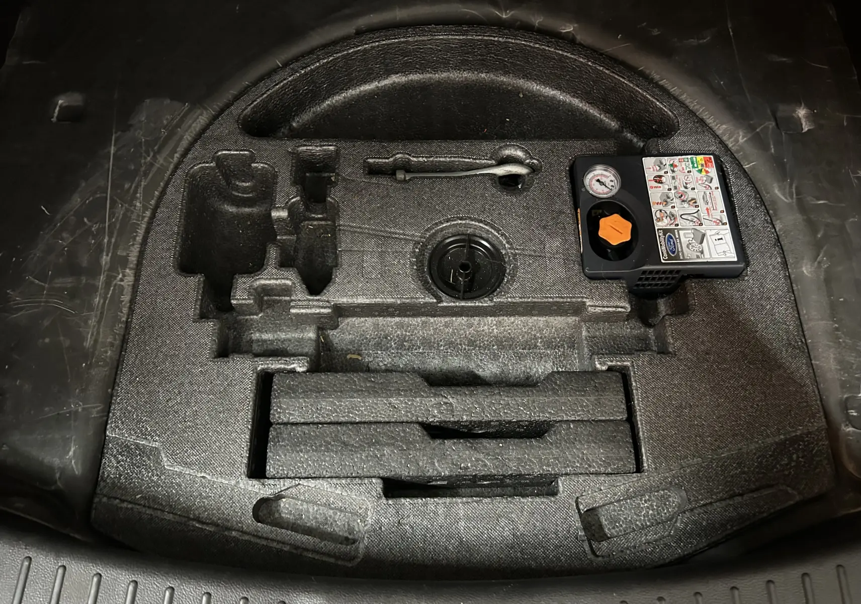Vue en plongée du compartiment de rangement noir sous le coffre du Ford Kuga 2017, avec kit de réparation pneus intégré.