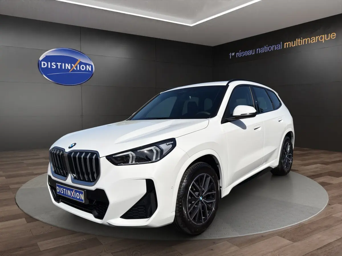 BMW X1 sDrive20d blanc vue 3/4 avant droit en showroom avec calandre noire et jantes foncées.