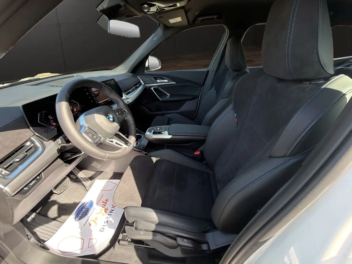 Vue intérieure côté conducteur du BMW X1 sDrive20d M Sport 2025, sièges noirs avec surpiqûres bleues et volant multifonction.
