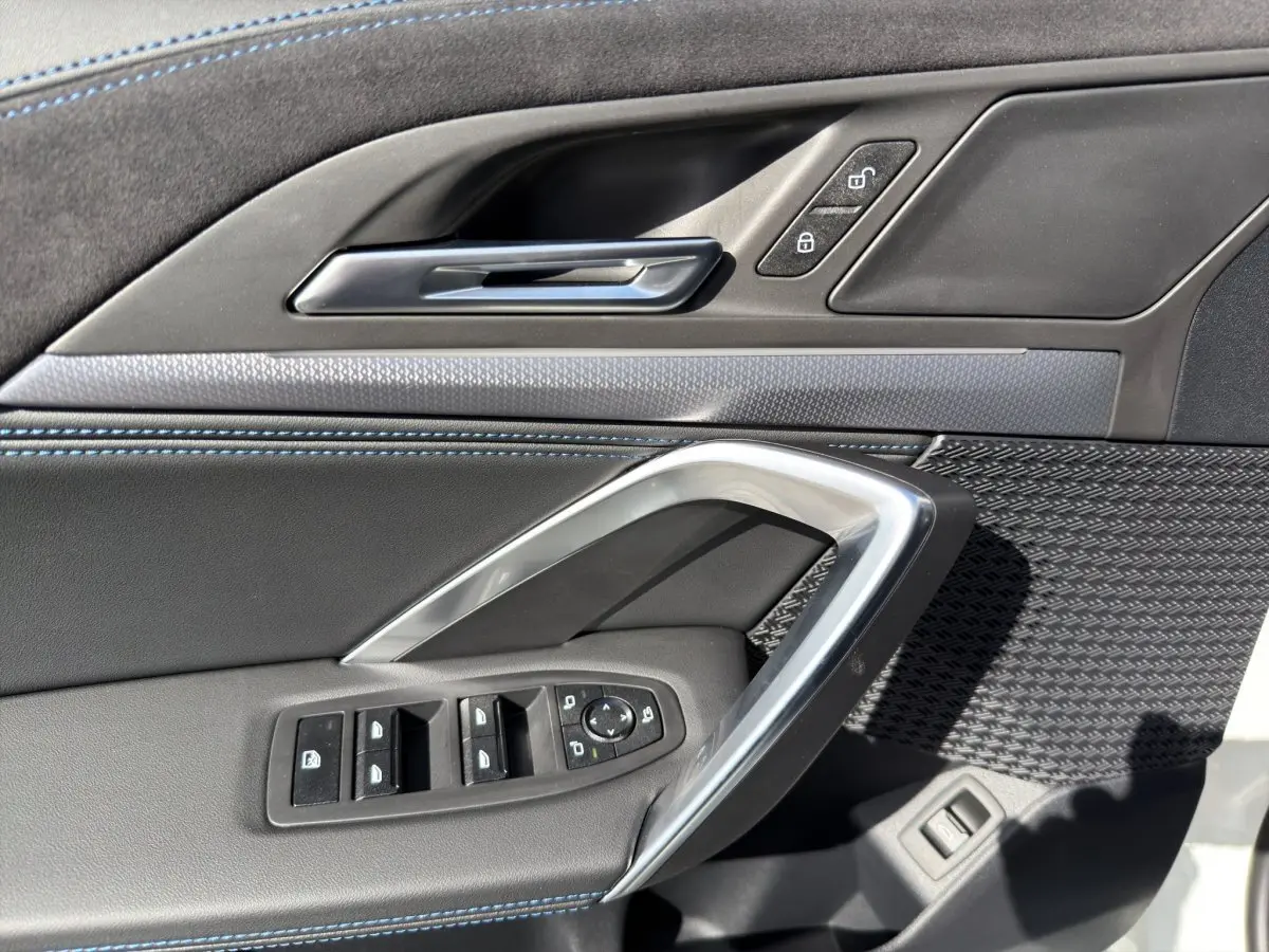 Détail de la porte avant gauche de BMW X1 blanc, avec commandes de vitres et poignée argentée.