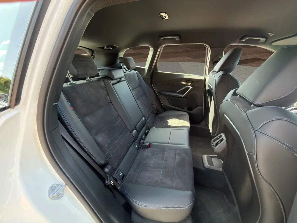 Vue intérieure côté droit des sièges arrière en cuir noir et alcantara avec surpiqûres bleues d’un BMW X1 blanc 2025.