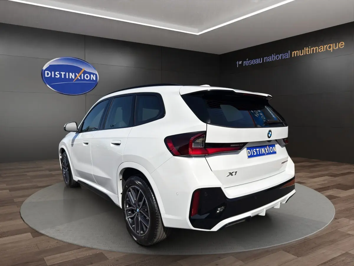 BMW X1 sDrive20d blanc vue 3/4 arrière droit avec jantes noires et feux arrière LED distinctifs.
