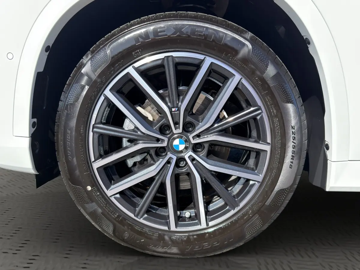 Gros plan sur la roue avant droite d'une BMW X1 blanche avec jante alliage M Sport et pneu Nexen.