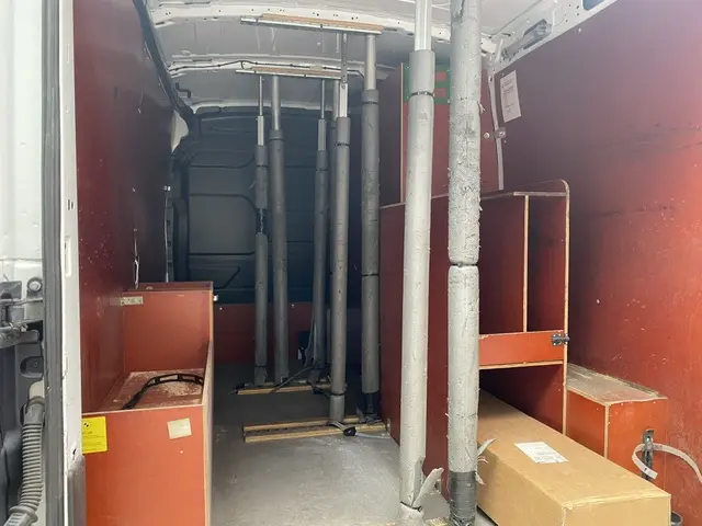 Intérieur du fourgon Ford Transit blanc vu de l'arrière, montrant l'aménagement avec cloisons et supports verticaux.