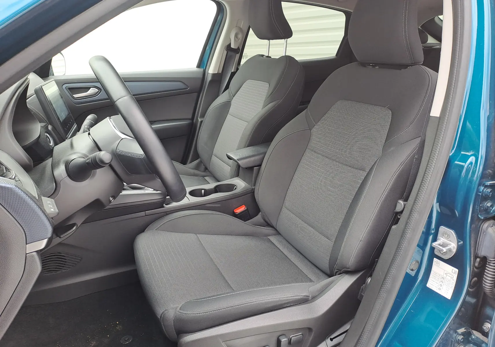 Vue intérieure côté conducteur du Renault Arkana bleu Zanzibar, sièges tissu noir avec réglages électriques visibles.