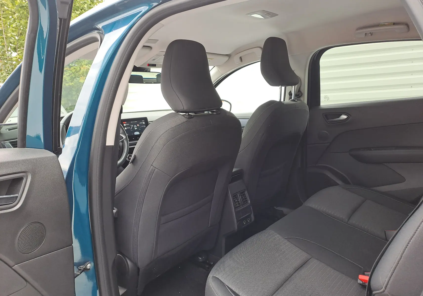 Vue intérieure arrière du Renault Arkana bleu Zanzibar, sièges tissu noir et console centrale avec aérateurs et ports USB.