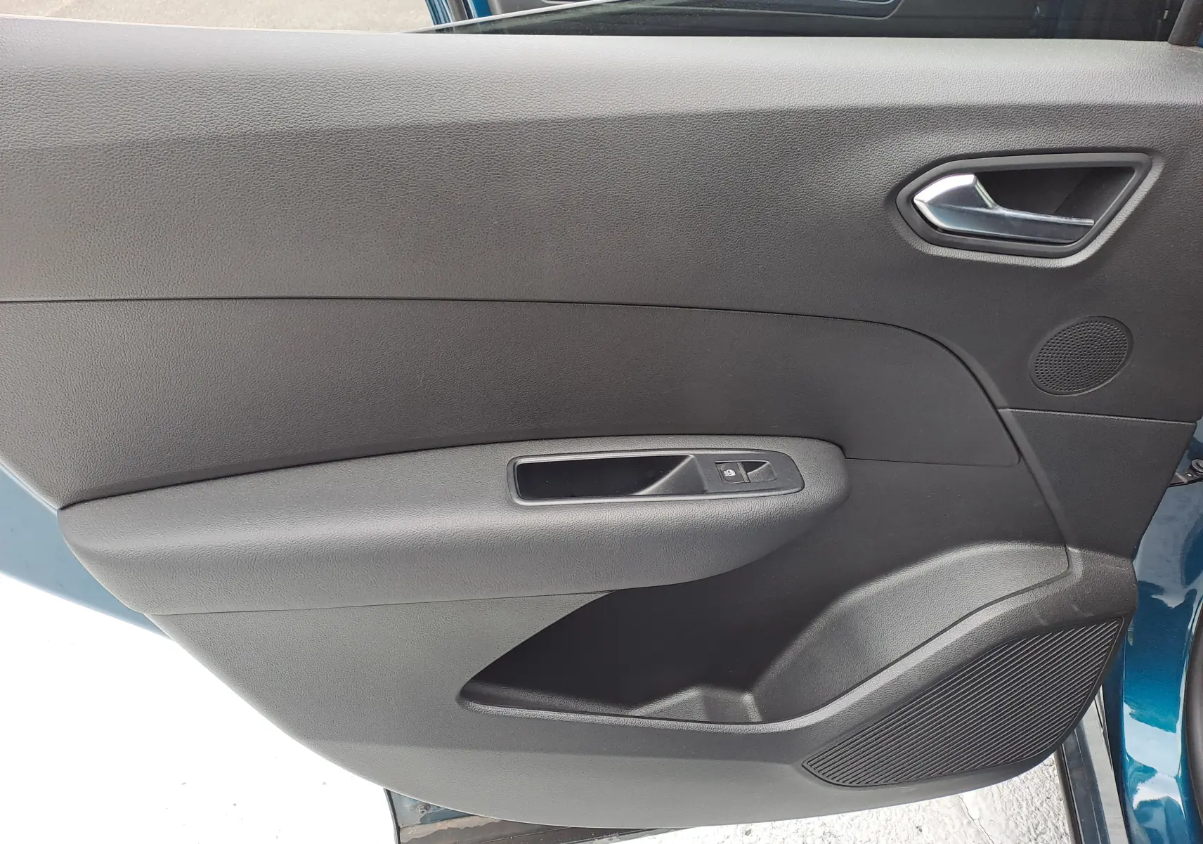 Intérieur côté gauche de la porte avant du Renault Arkana bleu Zanzibar, avec poignée argentée et commande de vitre.