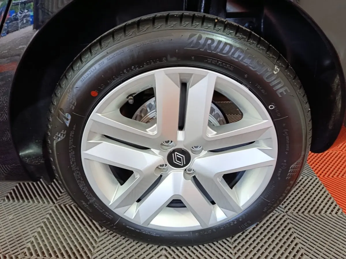 Gros plan sur la roue arrière gauche d'une Renault Clio 2025 couleur sombre, avec passage de roue et sol en damier rouge et gris.