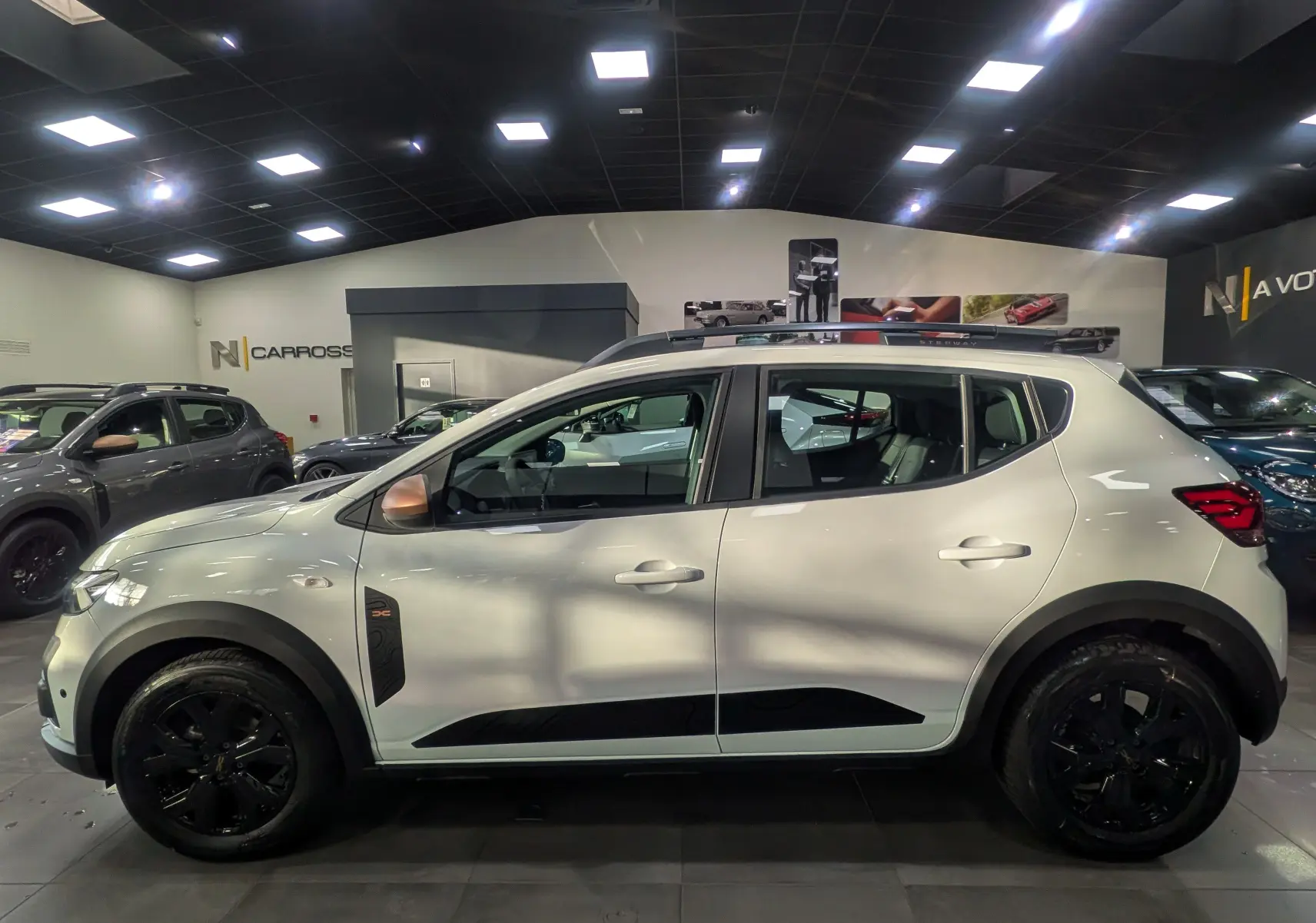 Profil côté gauche d'une Dacia Sandero Stepway TCe 110 blanche Glacier avec jantes noires et détails noirs contrastants.