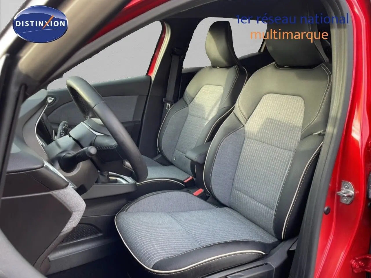 Vue intérieure côté conducteur de la Renault Clio rouge Désir Métal 2025, sièges tissu gris avec surpiqûres blanches.