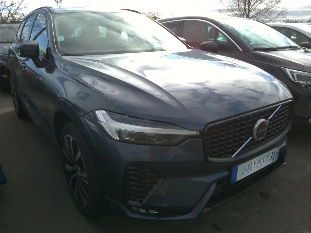 Vue 3/4 avant gauche d'un Volvo XC60 bleu avec calandre noire laquée et jantes alliage 20 pouces en Y.