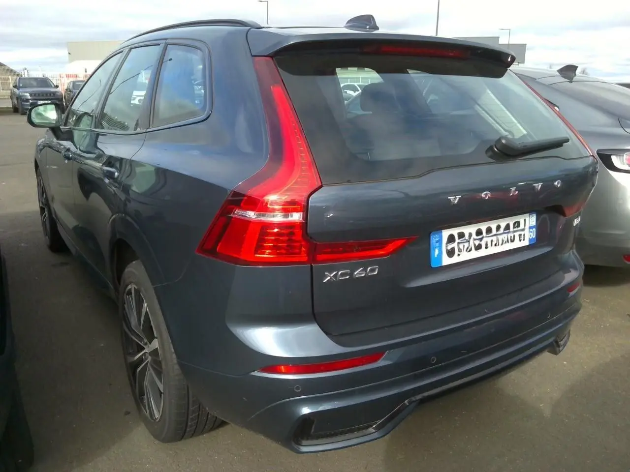 Vue 3/4 arrière droite d'un Volvo XC60 bleu avec feux arrière en forme de L et jantes alliage 20 pouces.