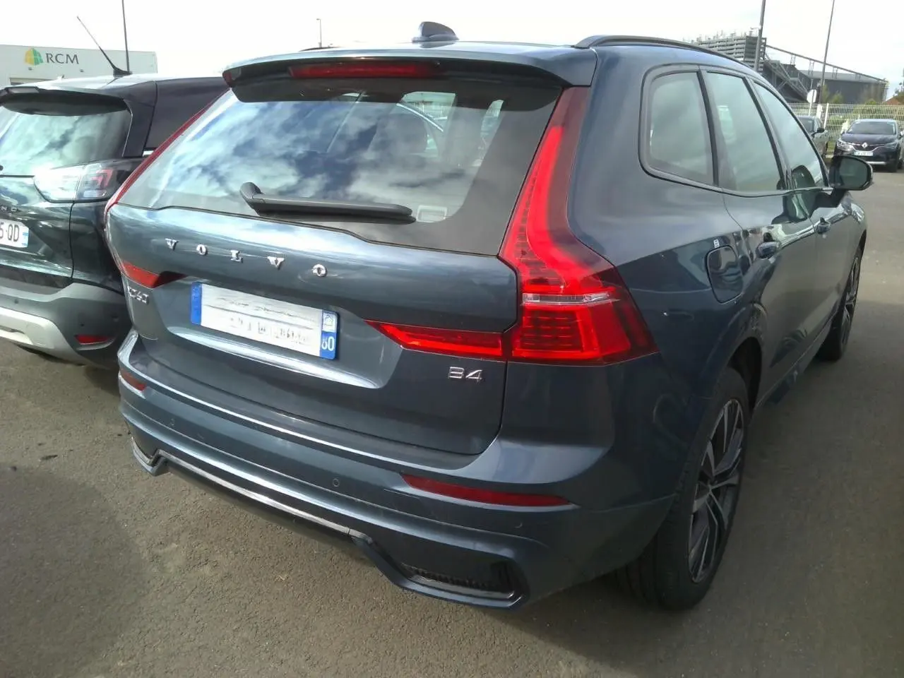 Vue 3/4 arrière droite d'un Volvo XC60 bleu avec feux arrière en forme de L et jantes alliage 20 pouces.
