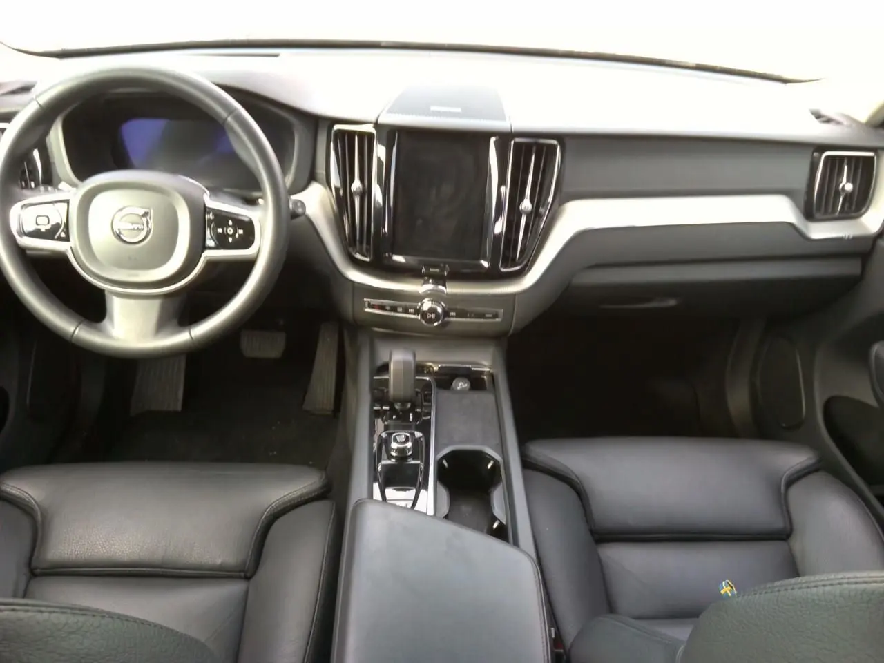 Vue intérieure avant du Volvo XC60 2023, tableau de bord et sièges en cuir noir avec console centrale moderne.