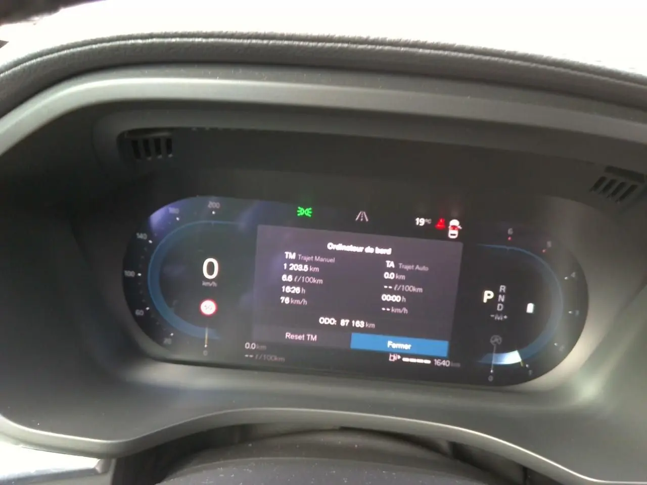 Gros plan sur l'ordinateur de bord numérique du Volvo XC60 bleu, affichant les données de trajet et la vitesse à 0 km/h.