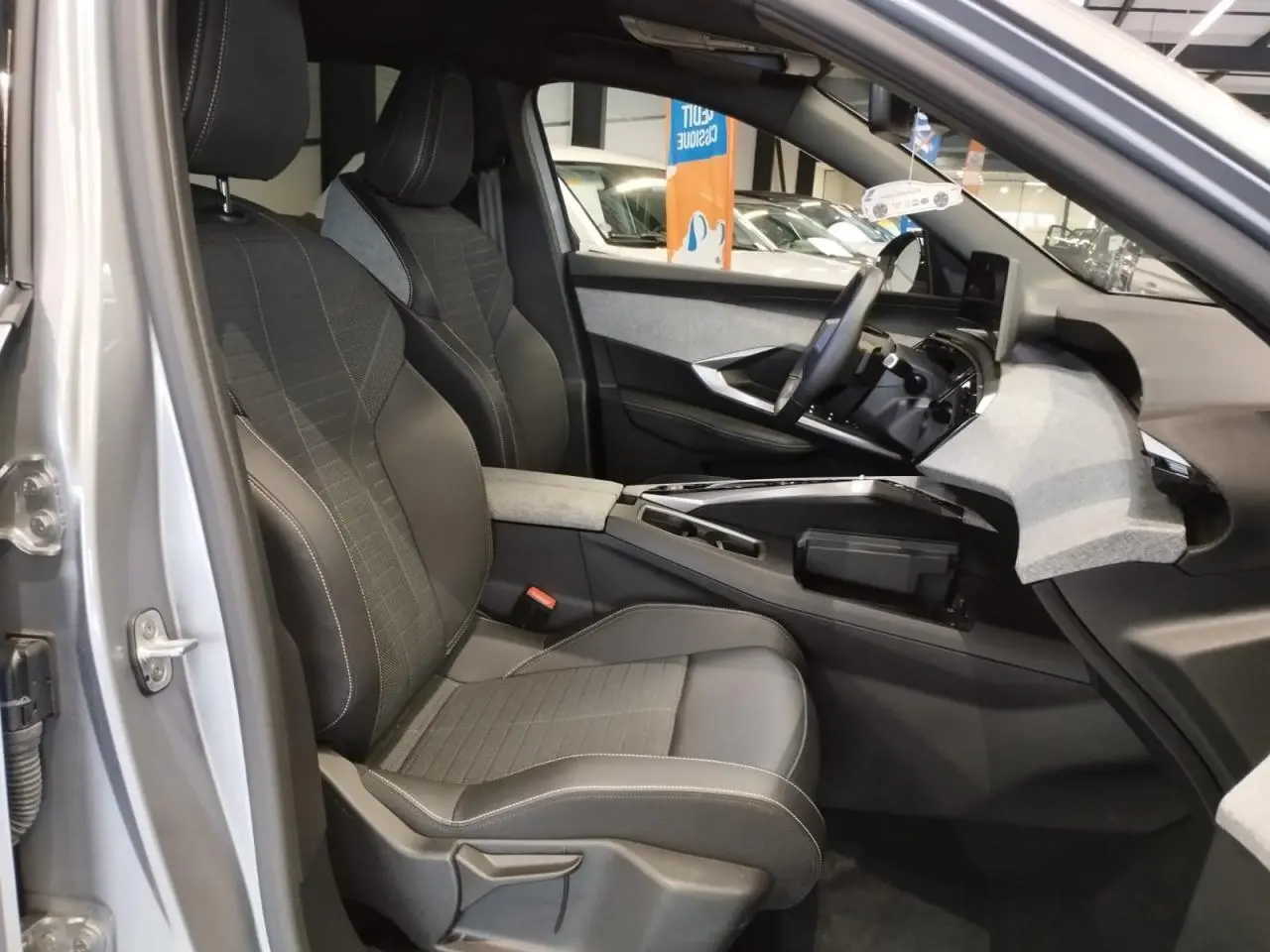 Vue intérieure côté conducteur du Peugeot 3008 gris Artense 2024, mettant en valeur les sièges et le tableau de bord moderne.