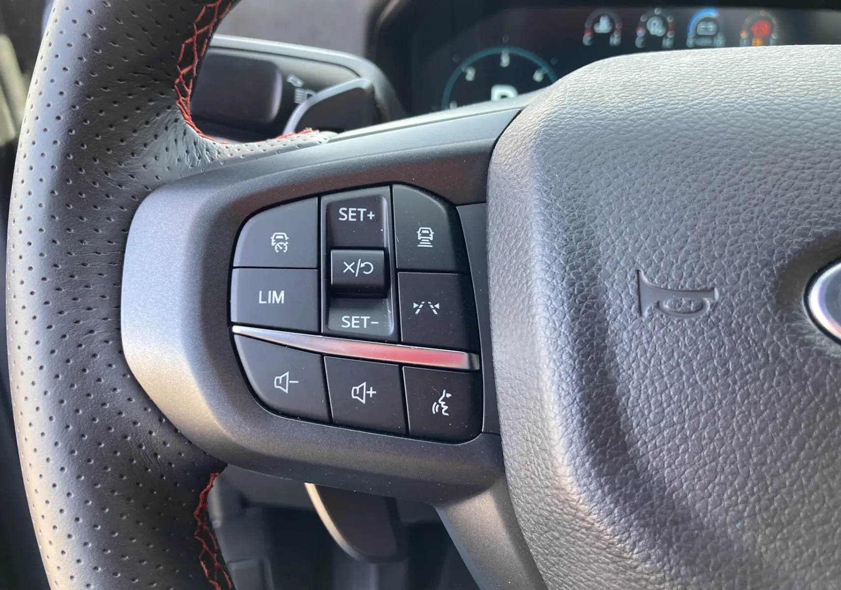 Gros plan sur le volant cuir perforé gris du Ford Ranger Raptor 2026, avec commandes multifonctions et surpiqûres rouges.