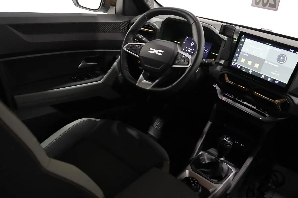 Vue intérieure côté conducteur du Dacia Duster 2024 avec volant multifonction, écran tactile et levier de vitesses manuel.