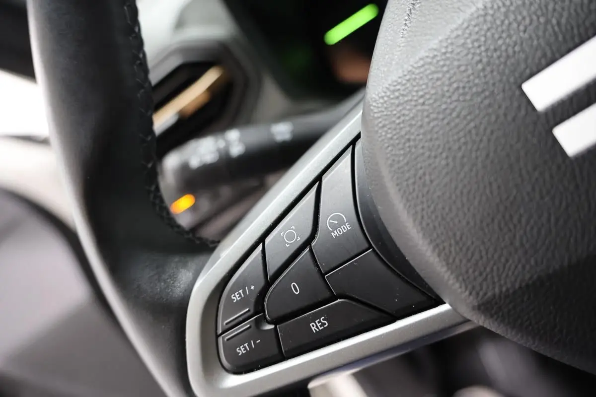 Gros plan sur les commandes au volant du Dacia Duster 2024, montrant les boutons de réglage et mode, intérieur noir.