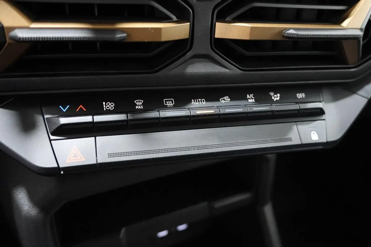 Gros plan sur la console centrale du Dacia Duster 2024, boutons de climatisation et ventilation avec inserts couleur sandstone.