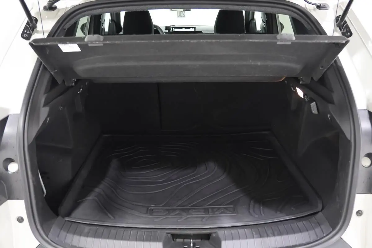 Coffre ouvert vu de l'arrière d'un Dacia Duster 2024 couleur Sandstone, tapis de coffre noir avec logo Dacia visible.